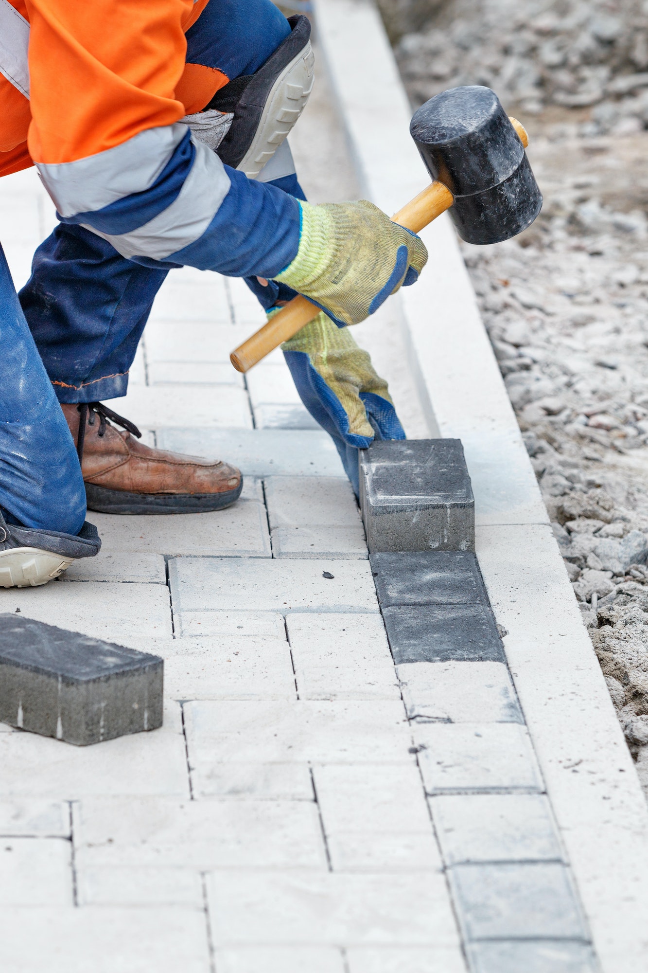 Vertical closeup of the worker banging the paving slabs with a rubber mallet.